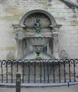 그랑플라스에서 약 100m 떨어졌으며 타운 홀의 왼쪽 골목으로 세번째 블럭쪽에 자그만 사거리에 오줌싸개 소년의 동상이 있다. 이 동상은 크기도 60cm정도로 작고 구석진 곳에 있어 다소 초라함이 느껴지기도 하지만 '브뤼셀의 가장 나이 많은 사람'으로 많은 시민의 사랑을 받고 있다.

이 동상은 1619년 제롬 뒤케노스에 의하여 제작 되어졌다. 이 청동상은 몇번이나 침략자들에 의한 약탈을 겪었지만 루이 15세는 당시 침략을 사죄하는 뜻으로 이 동상에 화려한 옷을 제작하여 선물하였고 그 이후 이 동상에게 걸맞는 의상을 세계 각국에서 보내옴으로서 세계최고의 옷 부자가 되었다. 또한 국빈이 방문하면 그나라의 전통의상을 입히는 것도 전례가 되었다.
예전에는 흔했던 식수용 분수중 하나였는데 벌거벗은 소년의 모습이 재미있어 시민들에의해 브뤼셀이 명물이 되었고 지금은 세계적으로 유명한 작품이 되었다. 또한 브뤼셀의 관광 토산품은 오줌누는 소년을 기점으로 많이 발전하게 되었고, 이로서 간단한 기념품을 구입하기엔 즐비하게 늘어선 주변의 가게를 찾으면 된다.